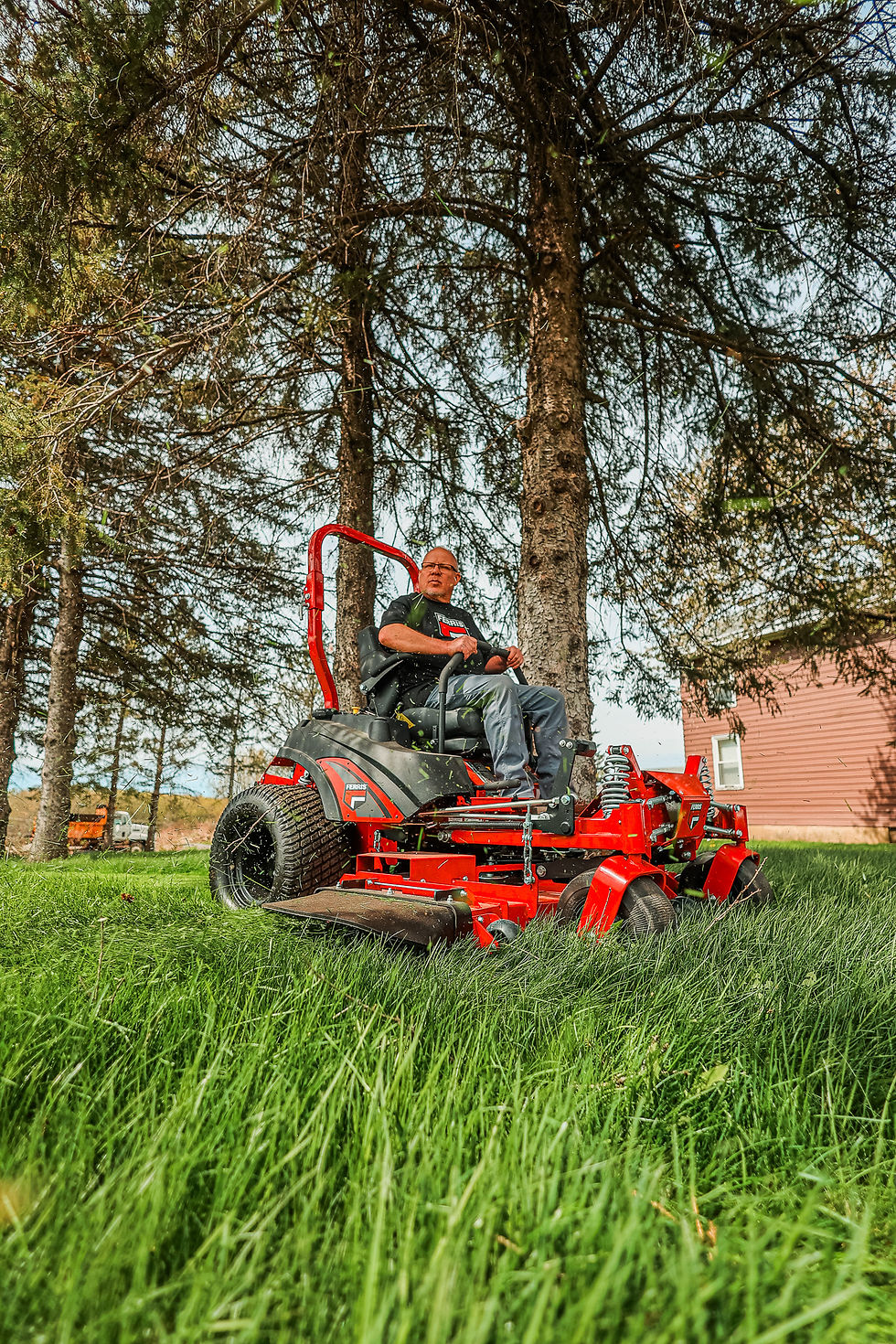 Man operating a red Ferris zero-turn mower cutting tall grass, sold and serviced by Clifton Equipment, a Ferris mower dealer near Syracuse New York