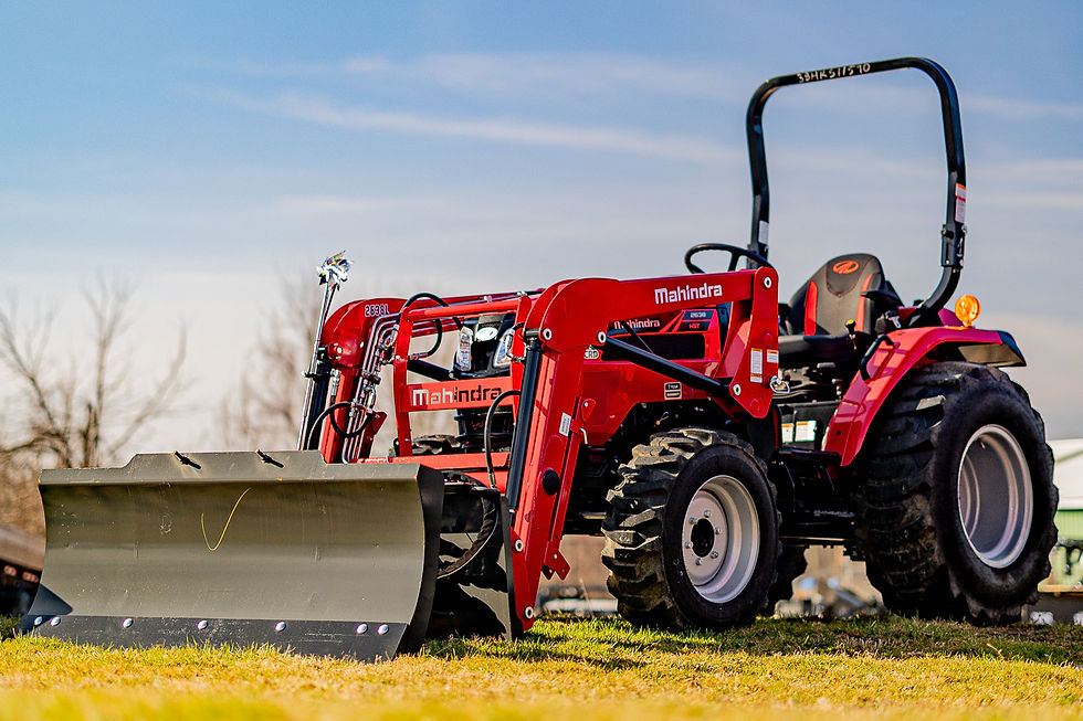 Red Mahindra tractor with front loader and blade parked on grass under a blue sky at the Clifton Equipment Mahindra dealership in Clay, NY.