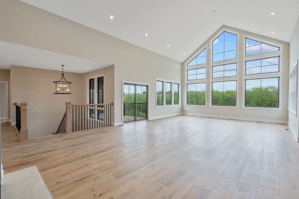 Spacious, empty room with large windows, wooden floors, and neutral walls. Bright natural light and scenic outdoor greenery visible.