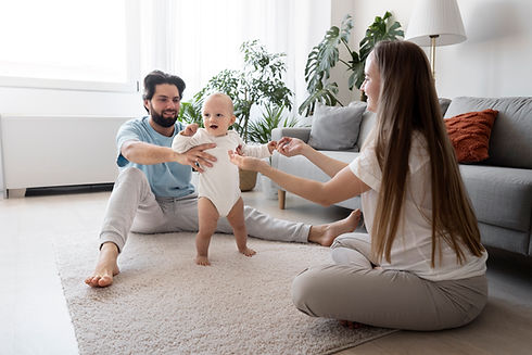 Parents watch as baby takes first steps in living room setting.