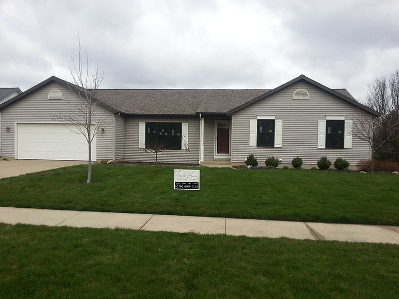 Gray house with white shutters, sign on lawn, cloudy sky background.