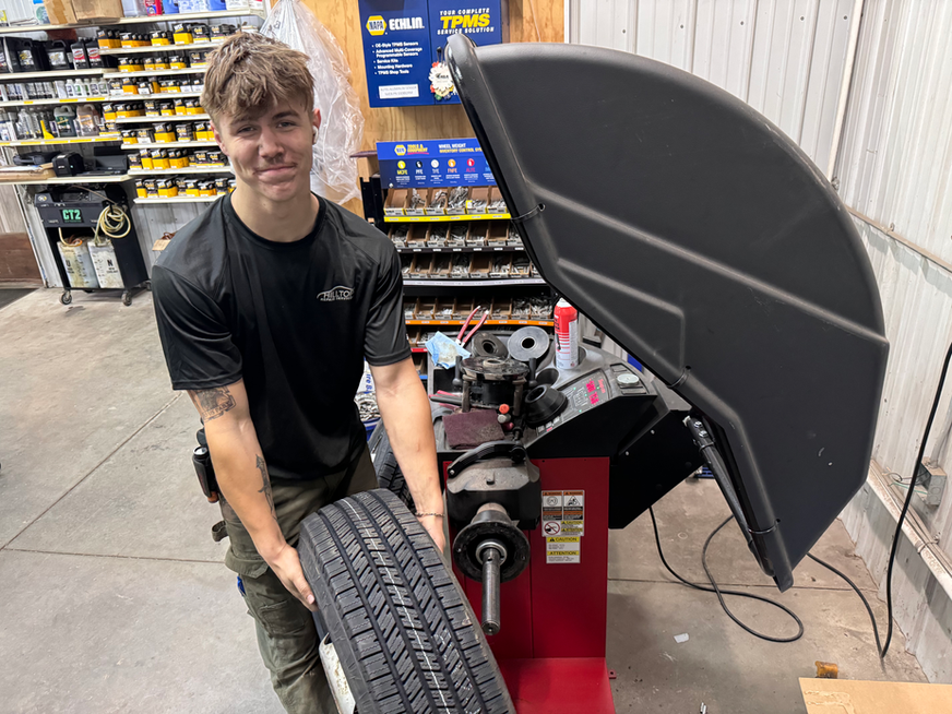 Man holding tire next to balancing machine in auto shop