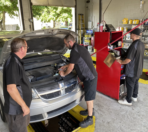 Three mechanics examining open car hood in a busy auto repair shop