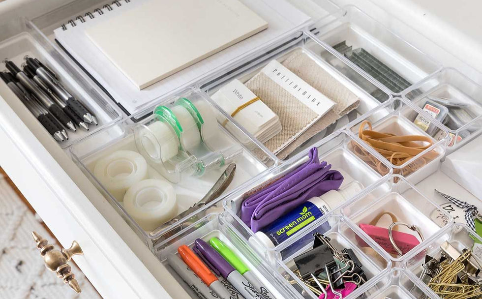 Organized drawer with acrylic organized compartments holding pens, tape, rubber bands, markers, glue sticks, and notebooks on a white background.