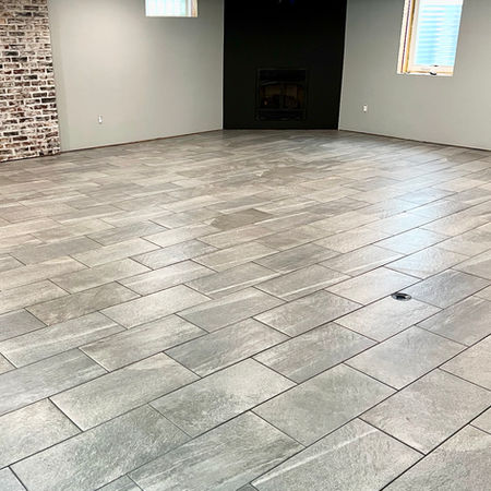 Gray rectangular tile floor in basement near brick wall and fireplace