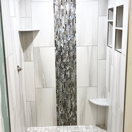 Shower with vertical multicolored glass mosaic band and marble-look tile