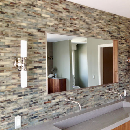 Multicolored glass tile backsplash with mirror and wall sconces