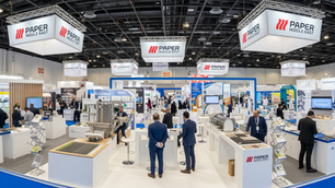 A dynamic horizontal view of the Paper Middle East Exhibition hall, showcasing machinery, various paper and packaging products on display, and attendees networking