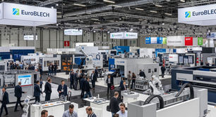Exhibition hall bustling with people at EuroBLECH event. Industrial booths, robotic machinery, and overhead signs in a modern setting.