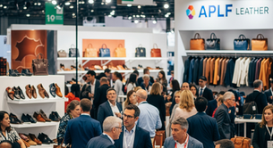 People socialize at a leather expo with shelves displaying shoes and bags. A sign reads "APLF Leather." The mood is busy and professional.