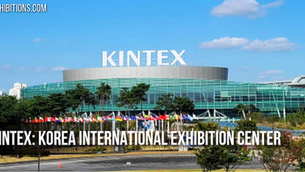 KINTEX building with large white text, Korea International Exhibition Center. Flags in front, blue sky, and lush greenery.