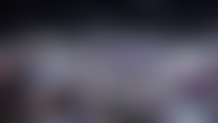 A bustling trade show in a large hall with numerous booths displaying electronics, illuminated signs, and a crowd exploring exhibits.