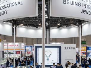 People explore a jewelry exhibition in a large hall with bright overhead lights. Signs read Beijing International Jewellery, creating a bustling atmosphere.