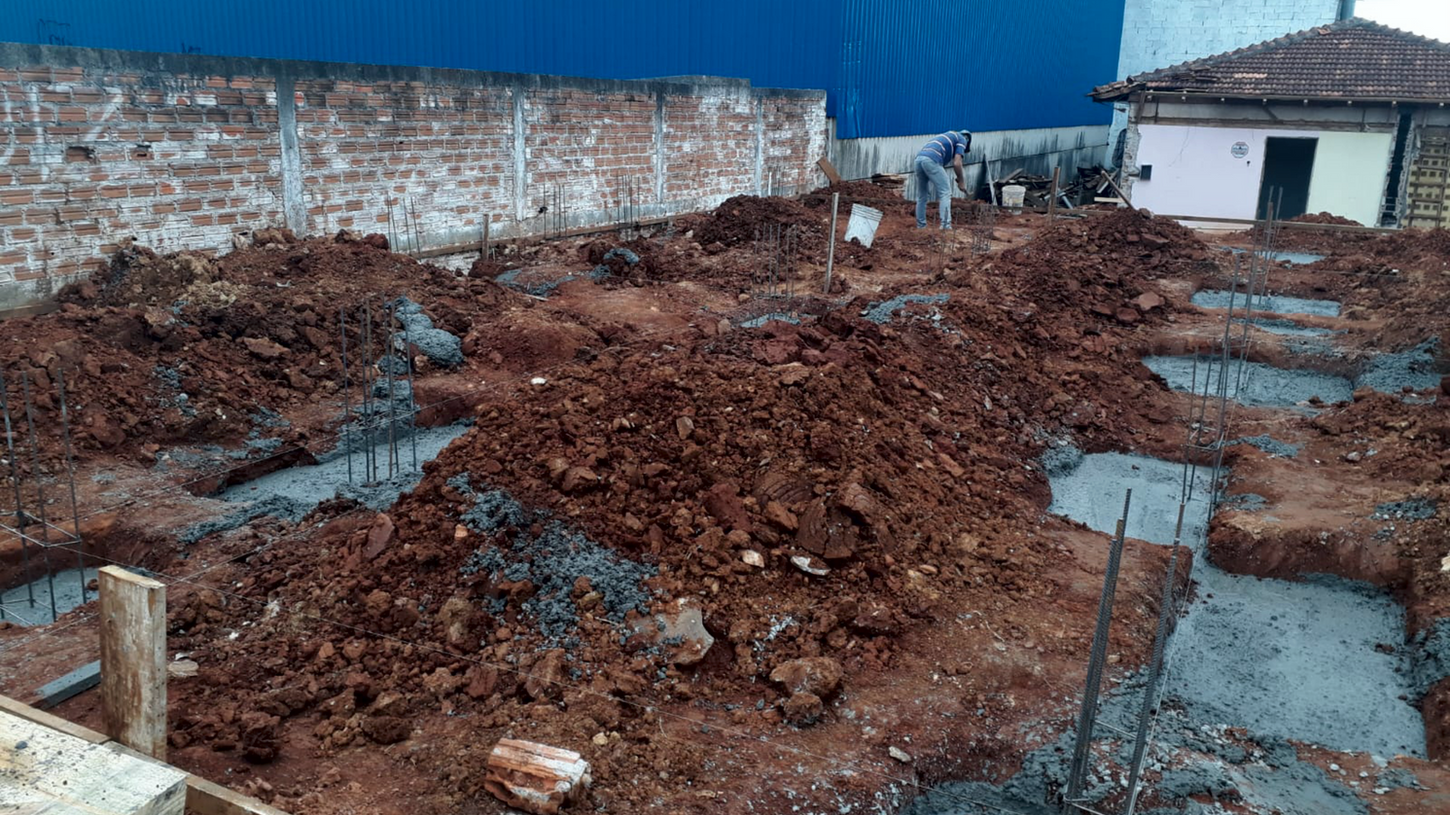 Construction site with dirt, foundations, and workers on the ground. Guara Construtora.