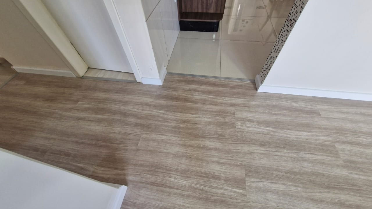 Interior view with wood-effect floor, white walls and doorway. Guara Construtora.