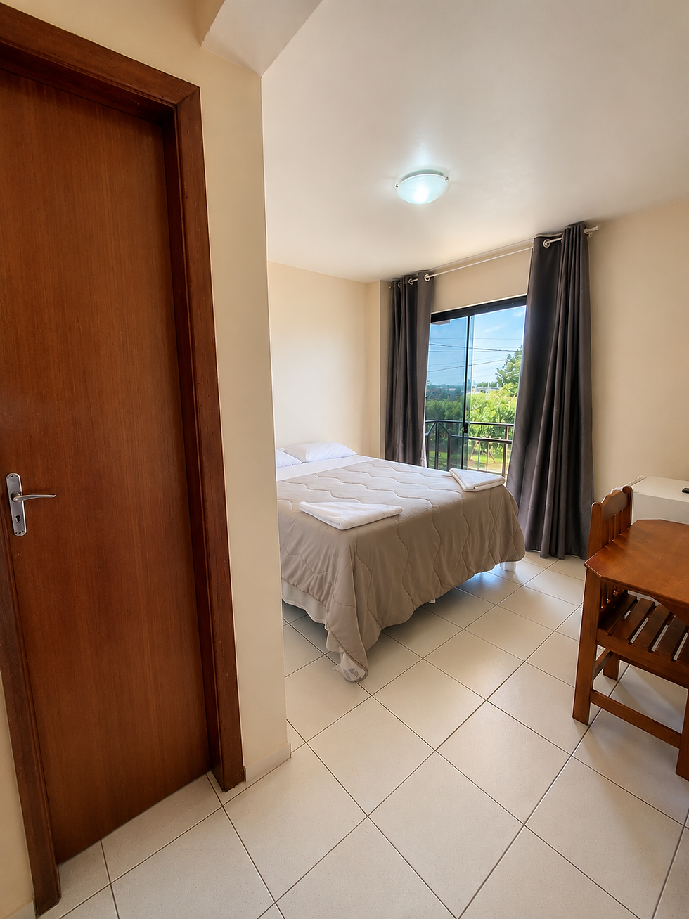 Quarto de hotel com cama de casal, janela e escrivaninha.