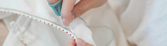 A person sewing white fabric with red tr
