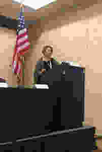 Woman standing at a podium and microphone, in front of a flag