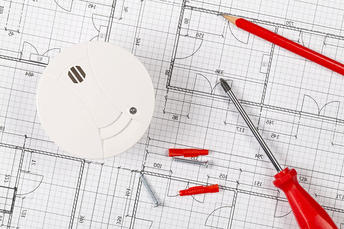 Smoke detector or fire alarm sensor on white architectural plans background with tools and