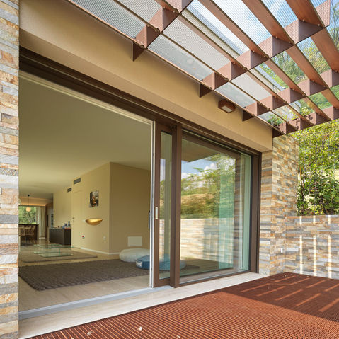 Portefinestre alzanti scorrevoli realizzate in legno di abete, con finitura laccata bianca nel lato interno e rivestimento esterno in alluminio color marrone scuro