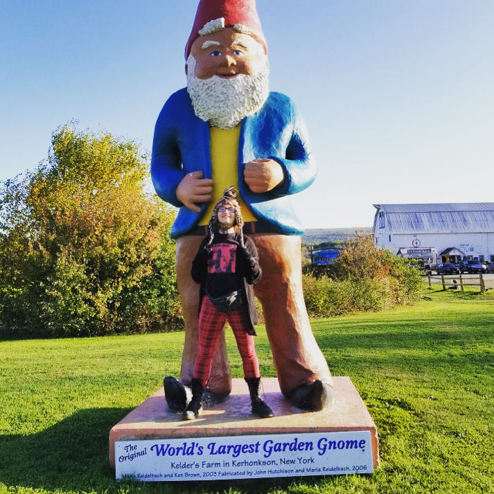 The author standing with a large gnome statue in their hometown in Upstate New York
