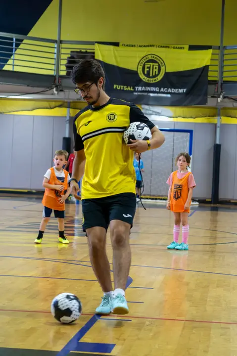 Coach holding Futsal balls while giving instructions to player in orange bib