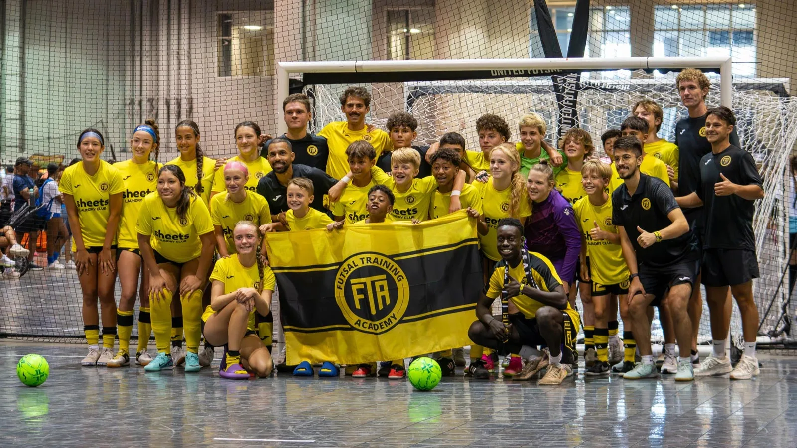 A group of players wearing a yellow futsal kit and holding a yellow FTA flag