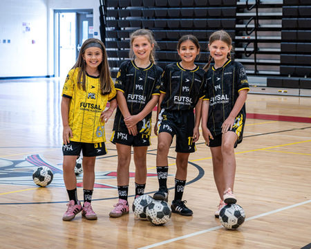 Four girls in futsal uniforms on an indoor court