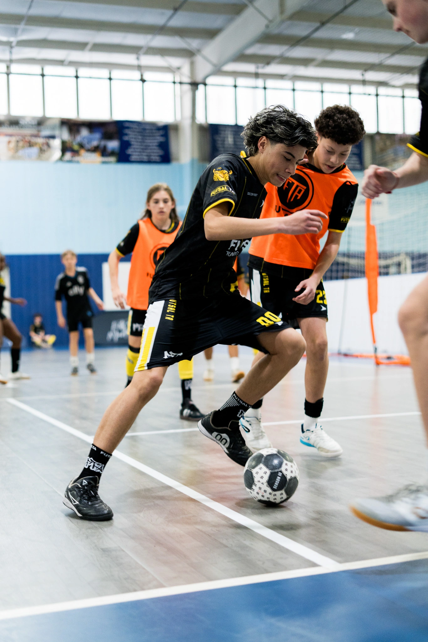Youth futsal player dribbling past defender during fast-paced indoor training session