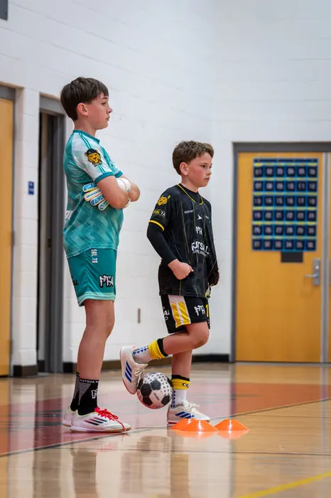 Two boys in soccer uniforms indoors, one with a ball