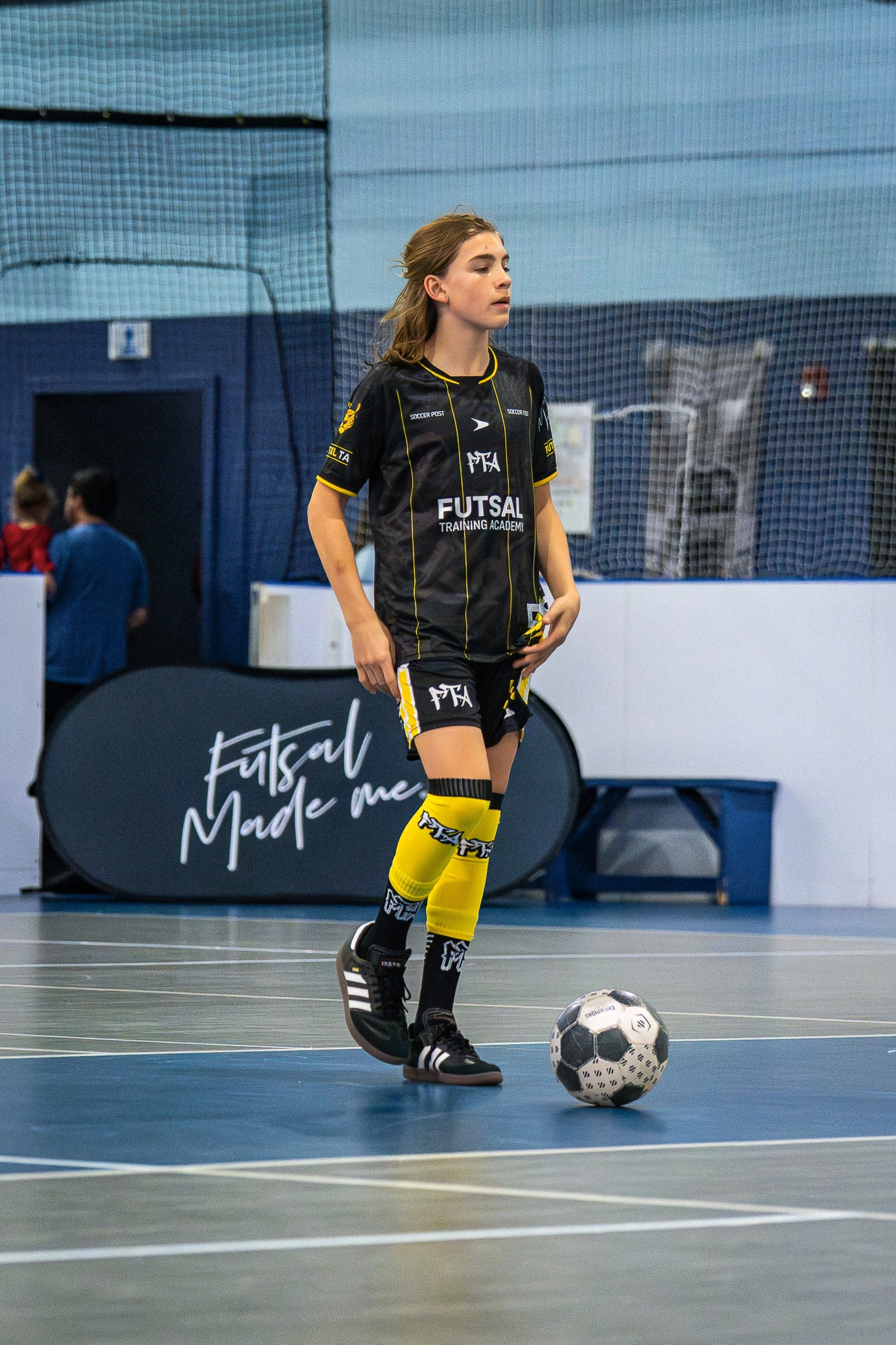 Youth futsal player in black and yellow Futsal Training Academy uniform controlling the ball during indoor match.