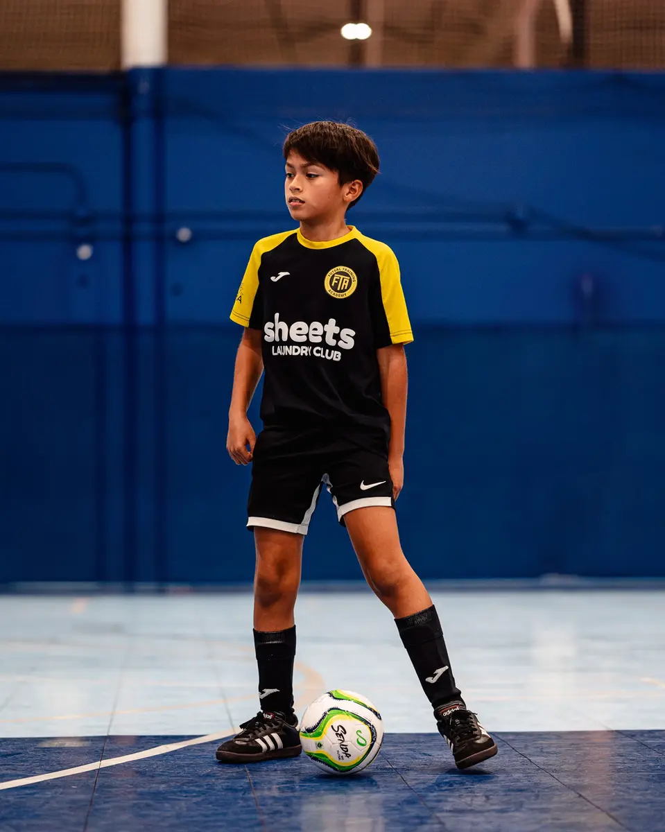 Young player in black training shirt and yellow socks dribbling the ball on indoor court