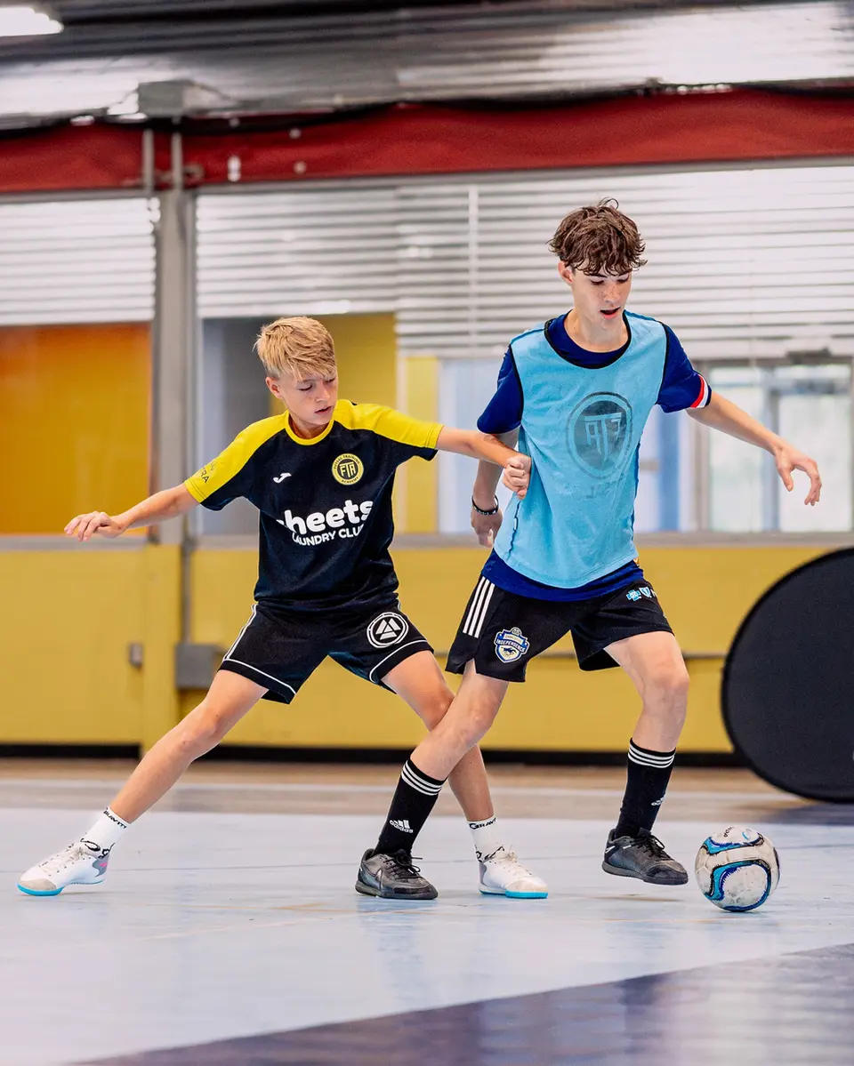 Two youth futsal players competing for the ball in a training session