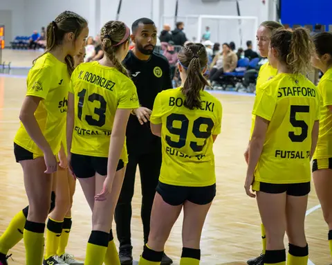 Three girls standing together, showing the backs of their custom Futsal TA jerseys