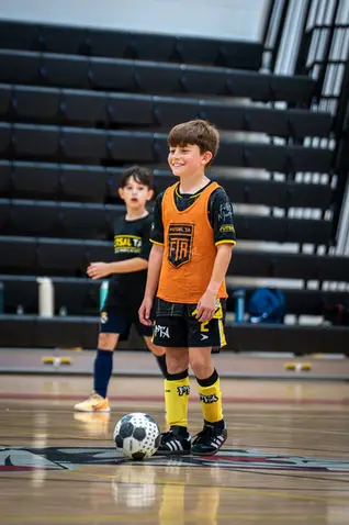 Smiling boy in orange soccer uniform with ball on court
