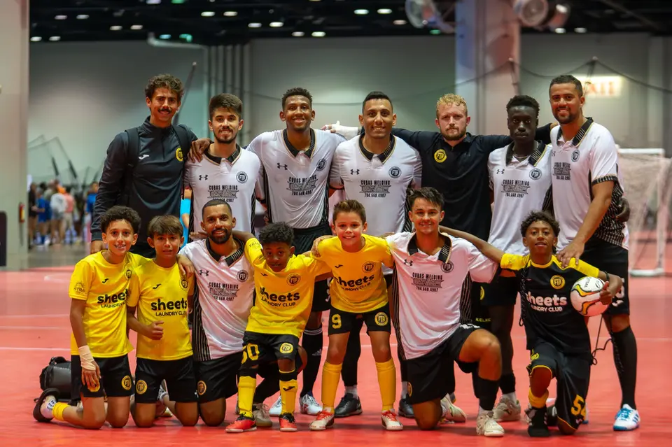 Mixed team of youth futsal players and adult coaches posing after a match on red court