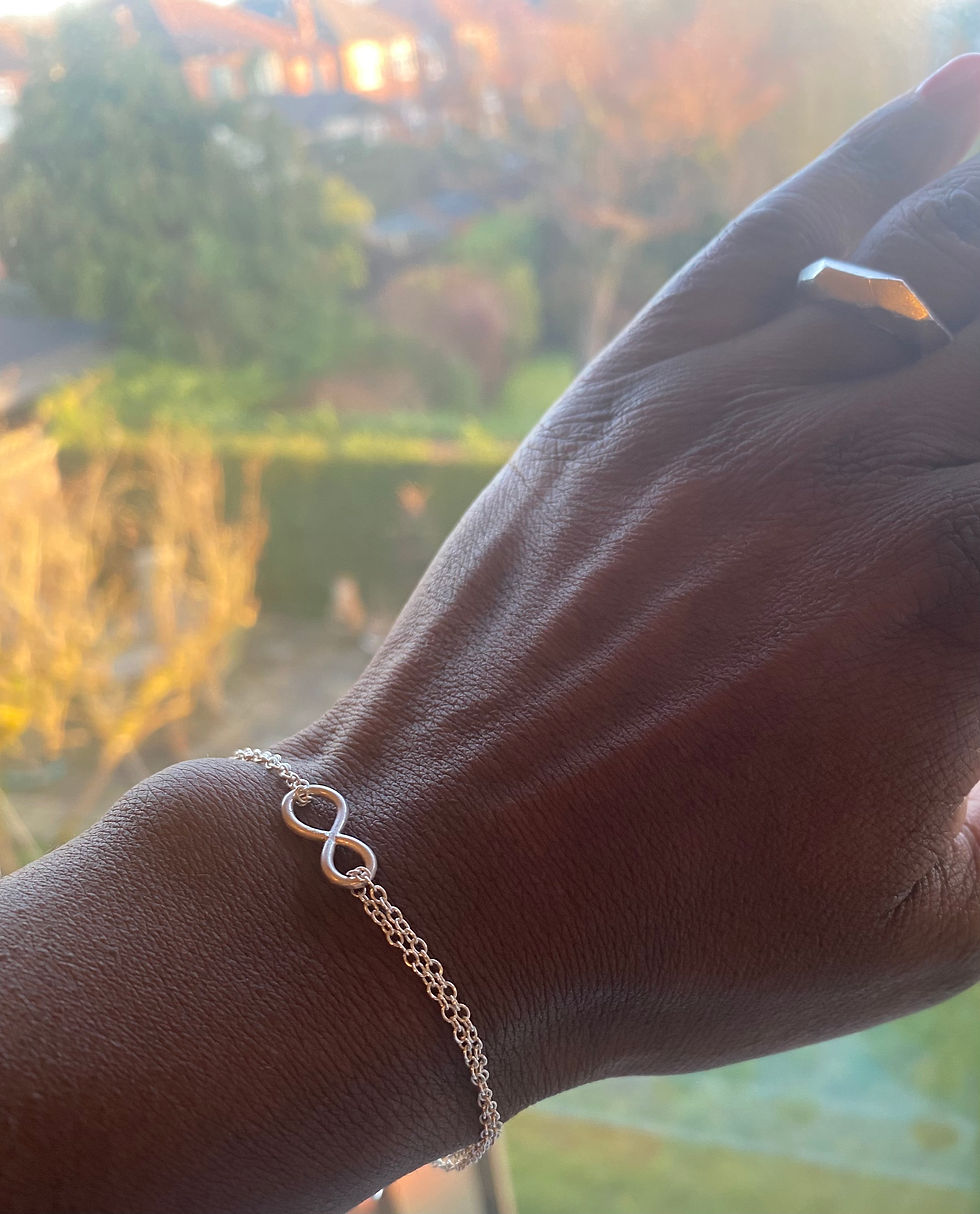Sterling silver double-stranded infinity bracelet on wrist, featuring an adjustable chain and polished infinity symbol.