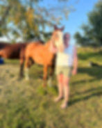 A brown horse standing over the shoulder of a lady wearing a white shirt
