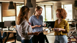 Three of the senior team discuss business over coffee in the middle of the office.