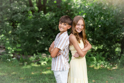 Brother and sister stand back to back in front of greenery during a family reunion photo session in Branson.