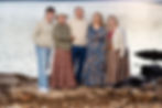Five smiling people in casual attire stand together on a rocky lakeside in Branson. Water sparkles in the background, evoking a serene, happy mood for their Branson Family photoshoot..