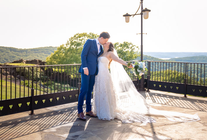 Bride flings out her bouquet with her arm in celebration while kissing groom wearing blue suit at Top of the Rock in Branson, MO