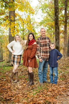 A family of four wearing autumn colors stands in a pile of colorful leaves in Branson, MO