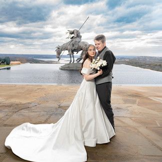 A couple embraces on a stone patio by an infinity pool, with a horse statue in the background at Top of the Rock in Branson. Bride in white dress holding bouquet at Top of the Rock in Branson