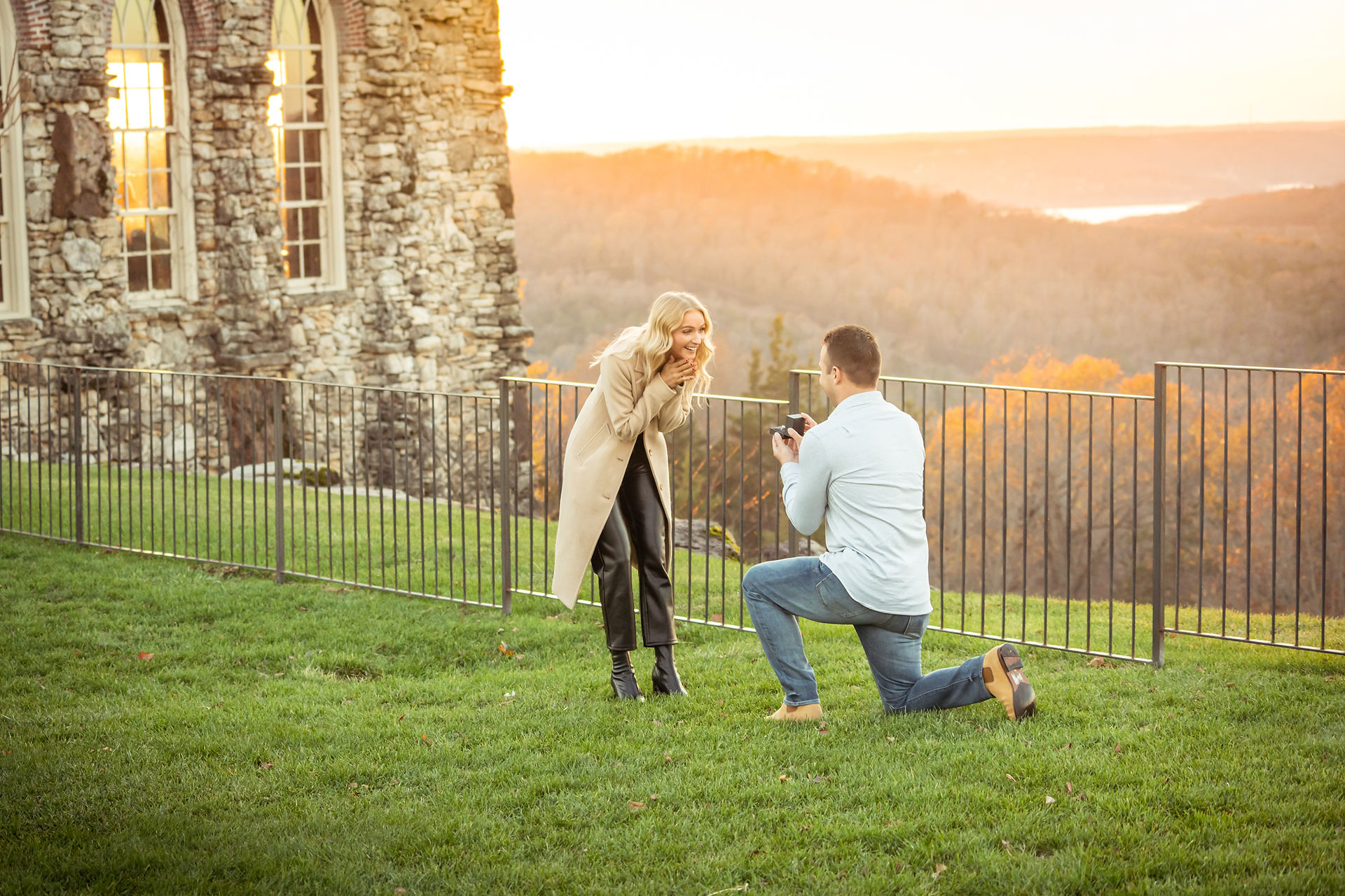 A man down on one knee proposes to surprised girlfriend in front of the Chapel of the Ozarks at Top of the Rock