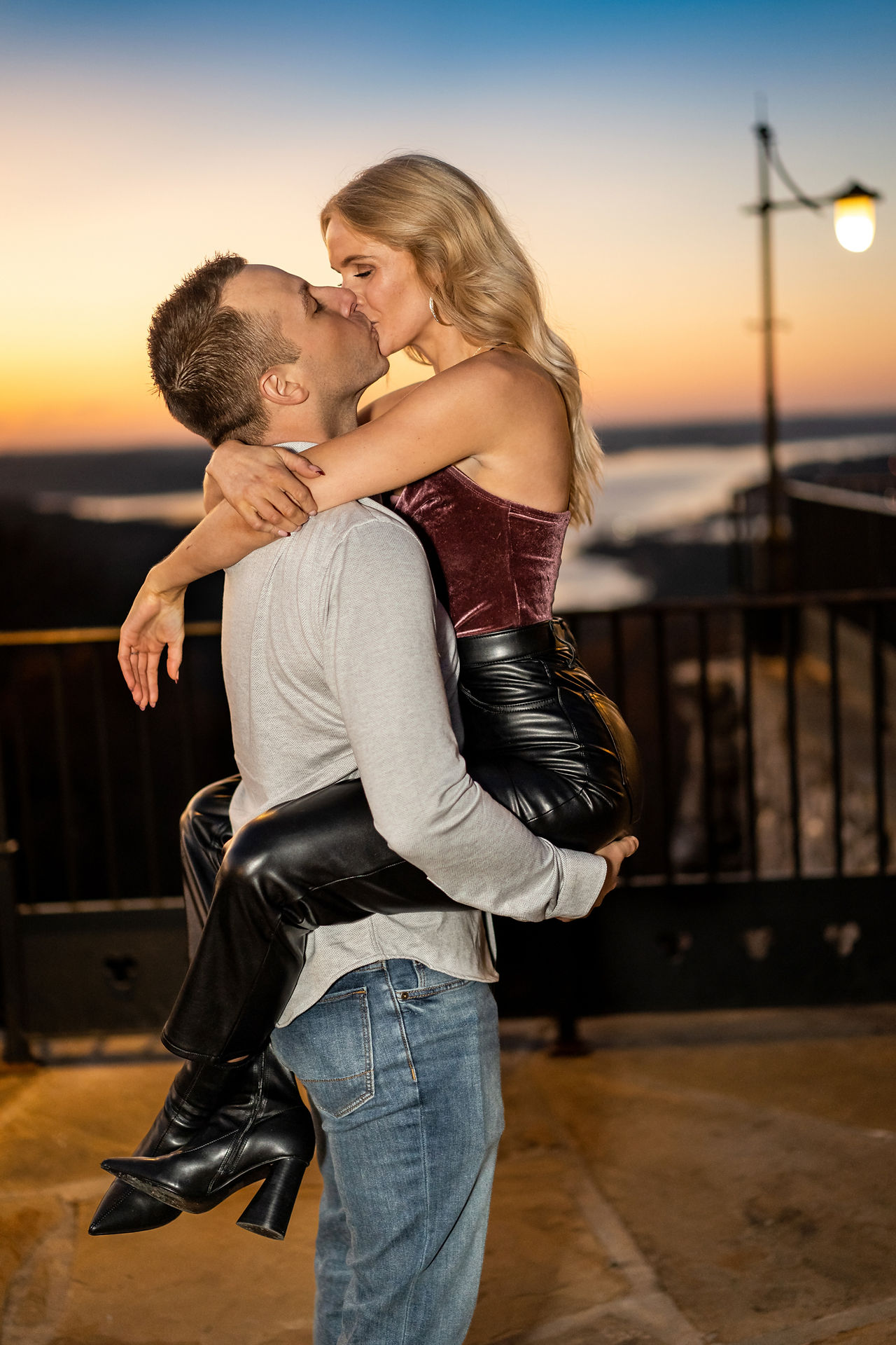 Man picks up his new fiancé and she wraps her legs around him at sunset at Top of the Rock 