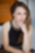 Professional female wedding and family photographer in a black shirt leans forward with a gentle smile, showcasing blue nail polish and a confident, approachable expression.