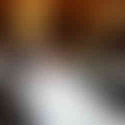 Bride cuddles up to her groom with her legs on him in an elegant room; the woman wears a white gown, leaning calmly. A table with candles and flowers adorns the background.