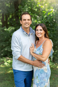 Husband and wife embracing during extended family photos in Branson among natural greenery.