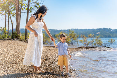 Mom and young son walk hand in hand beside the blue water of Table Rock Lake with the Ozark hills in the background